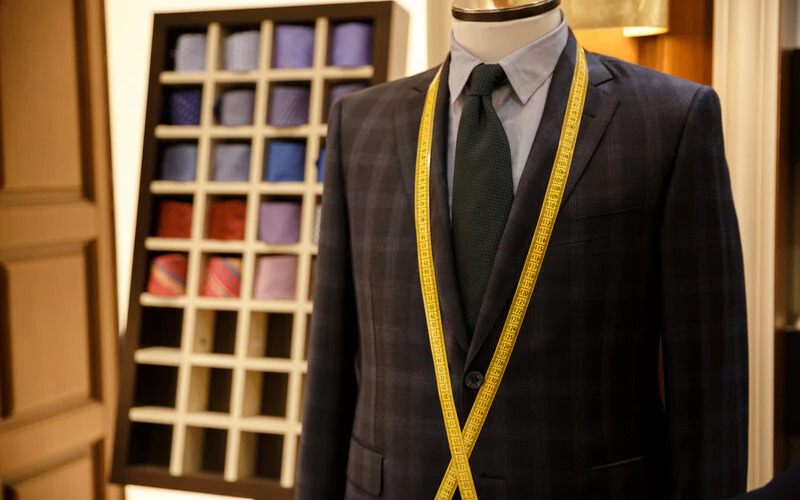 A custom Pearce Bespoke tailored suit on a mannequin with measuring tape draped across it.
