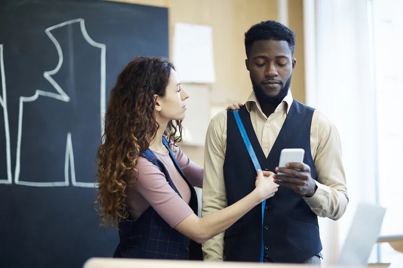 A woman measuring a bespoke suit for a business man - Expanding Clientele through Our Bespoke Custom Suit Franchise with Pearce Bespoke 