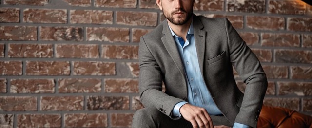 A man sitting down, wearing a light gray custom suit